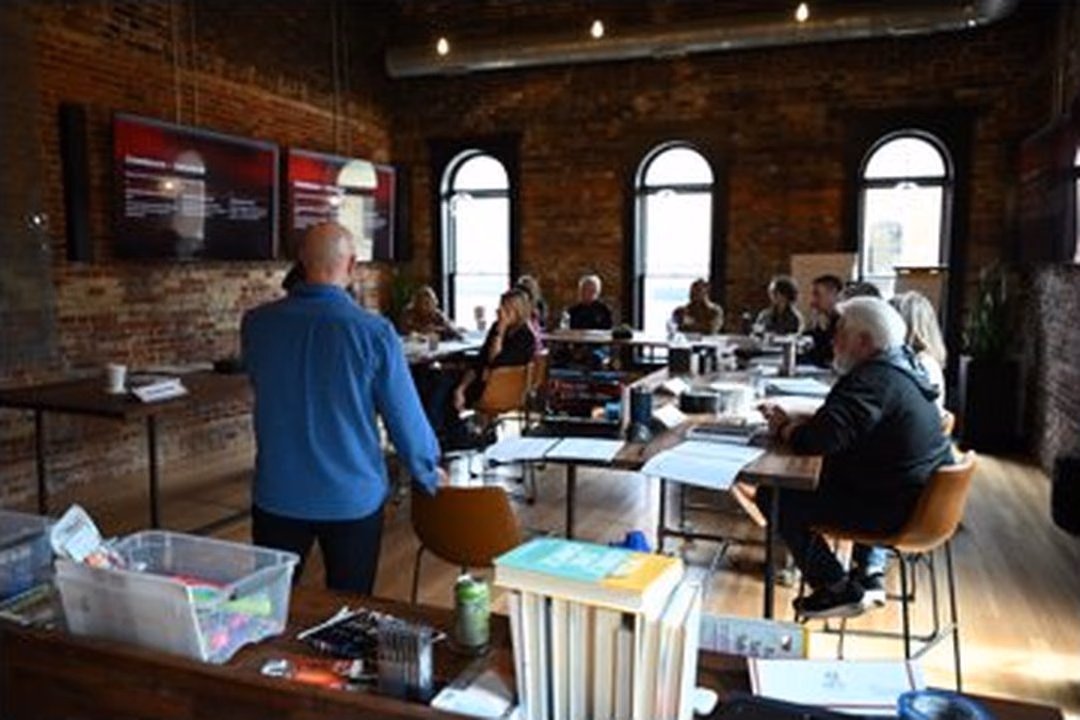 Niels standing at the front of a brick-walled room in Stillwater, a leadership team at long tables listening