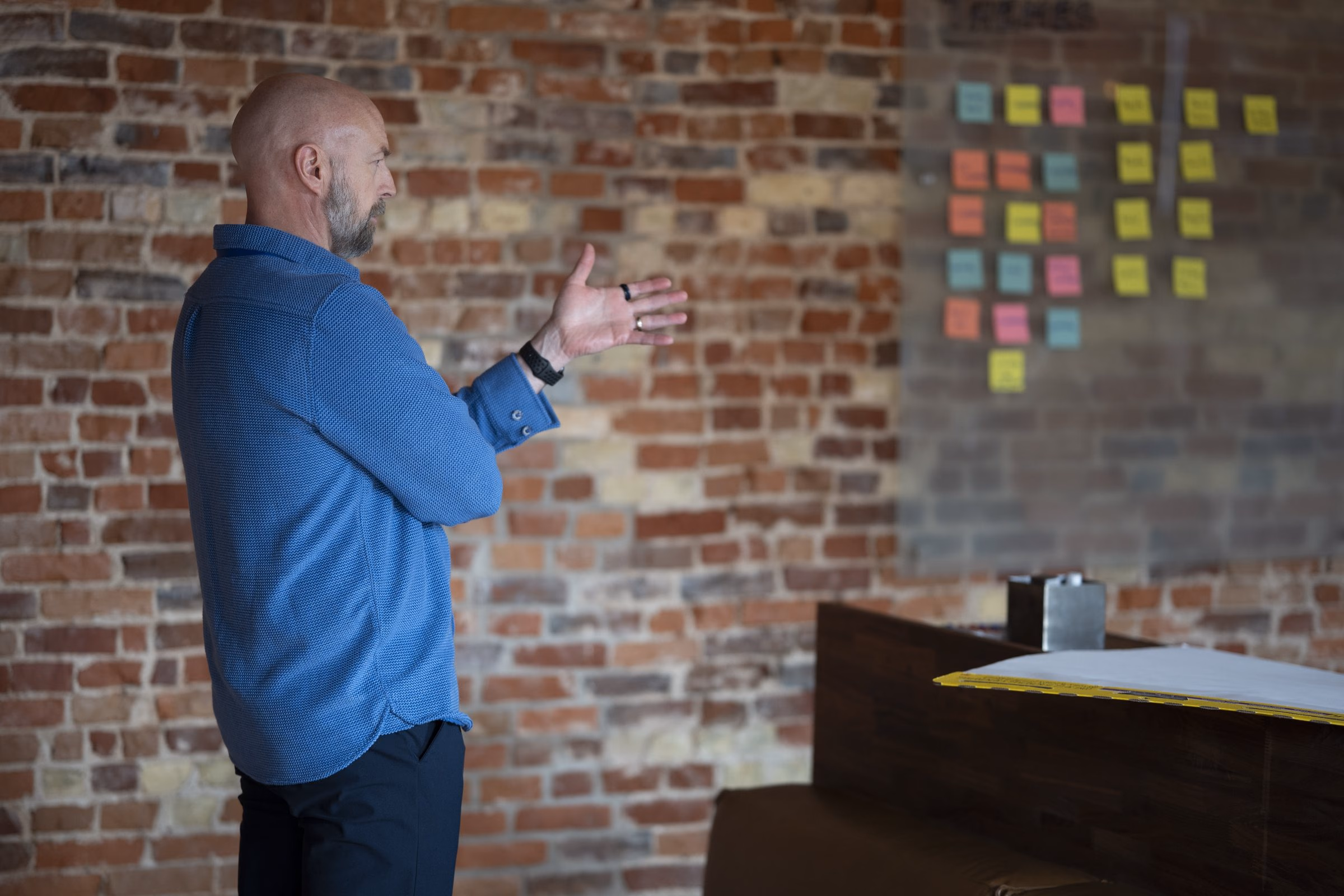 Niels at a brick wall covered in colored sticky notes, arm extended, working through the themes