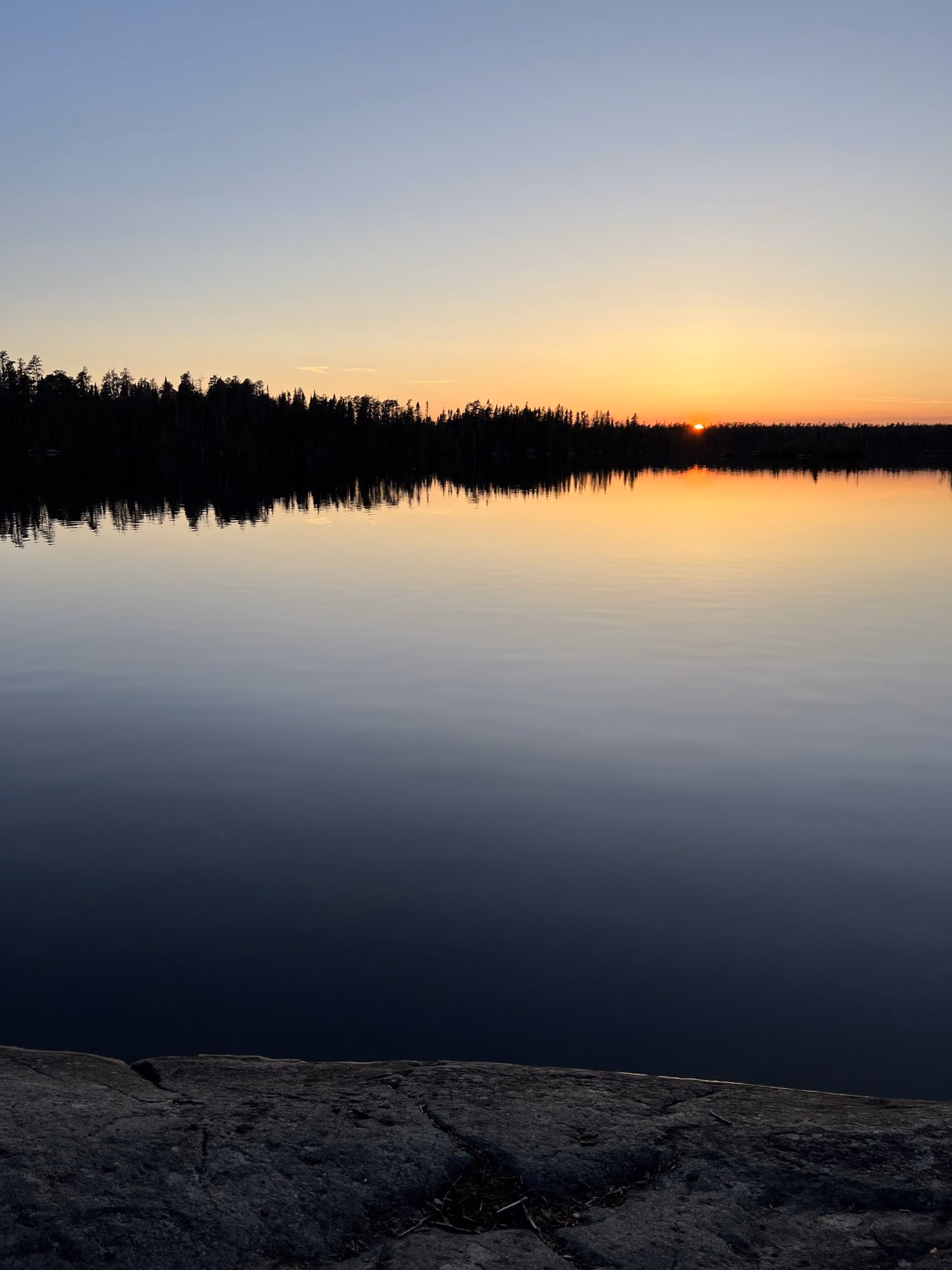 Dusk over a glassy lake in the Boundary Waters, the tree line black against a gold sky