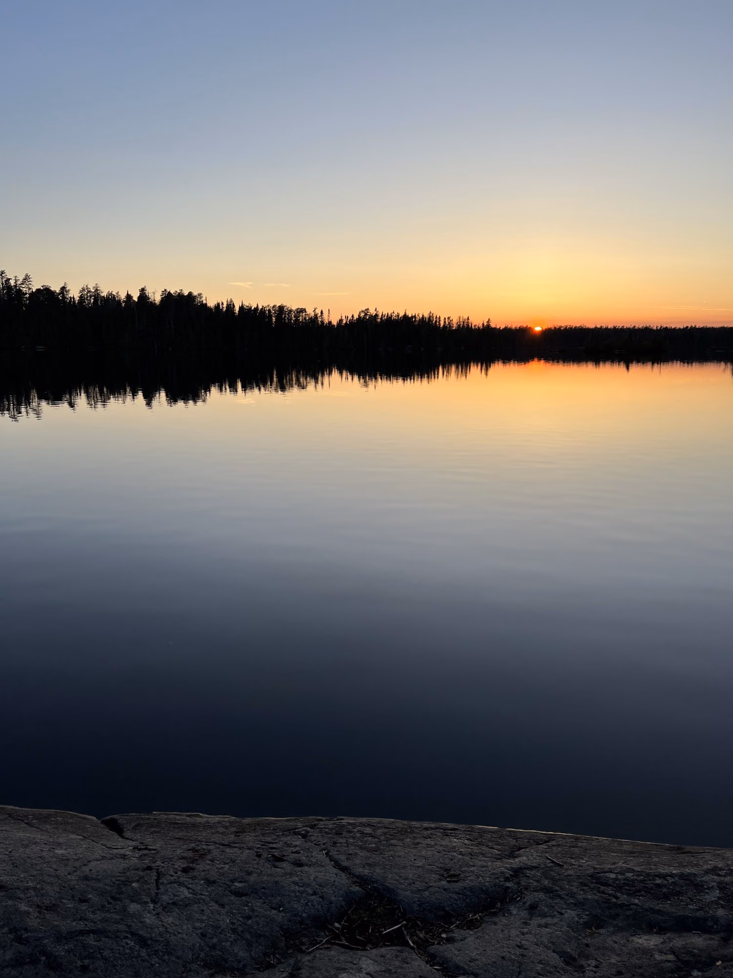 Dusk over a glassy lake in the Boundary Waters, the tree line black against a gold sky
