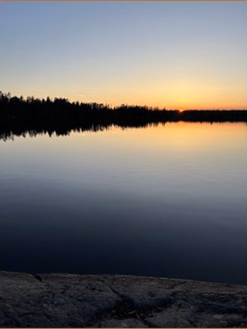 Dusk over a glassy lake in the Boundary Waters, the tree line black against a gold sky
